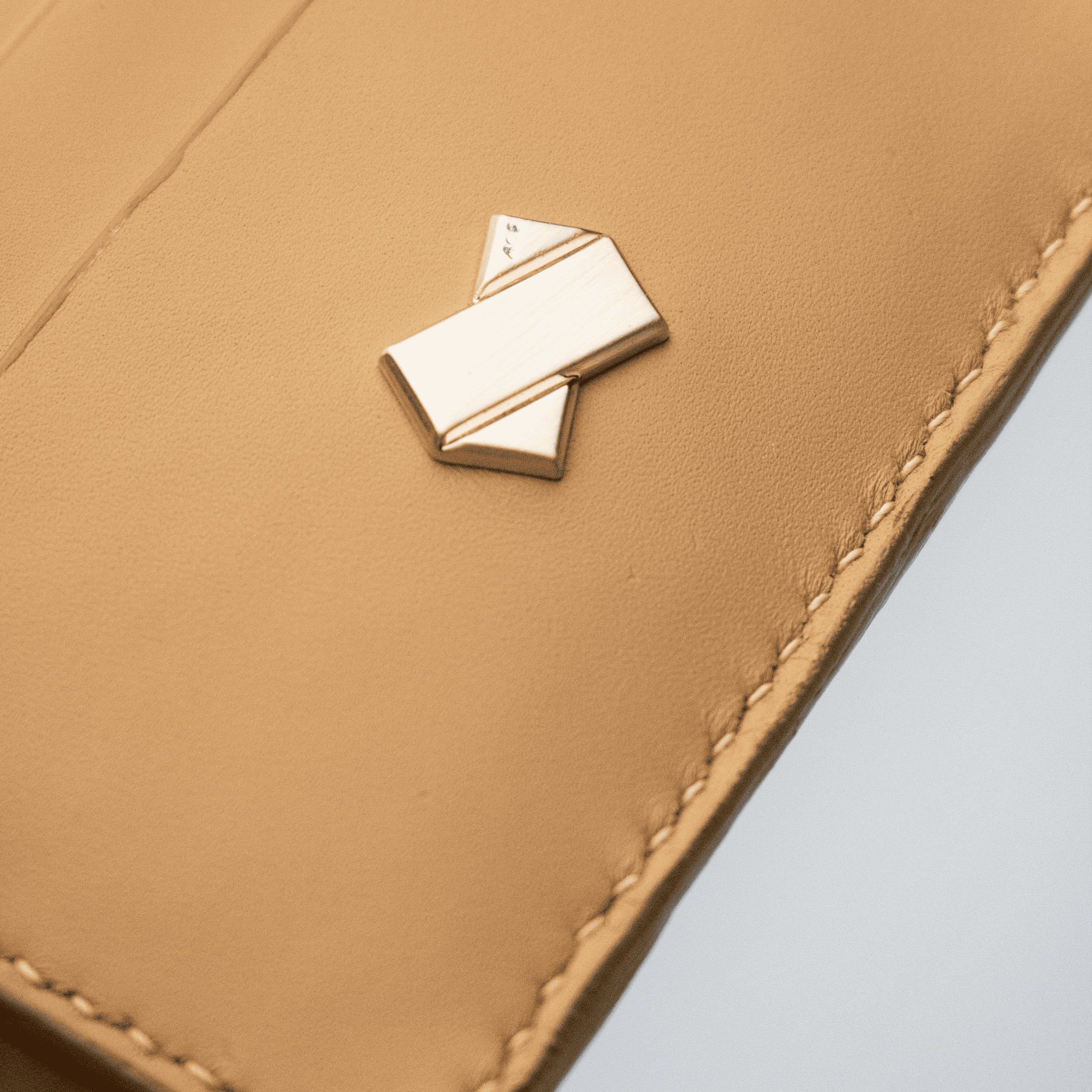 Nærbillede af det gyldne Faubret-logo på det glatte camel læder.