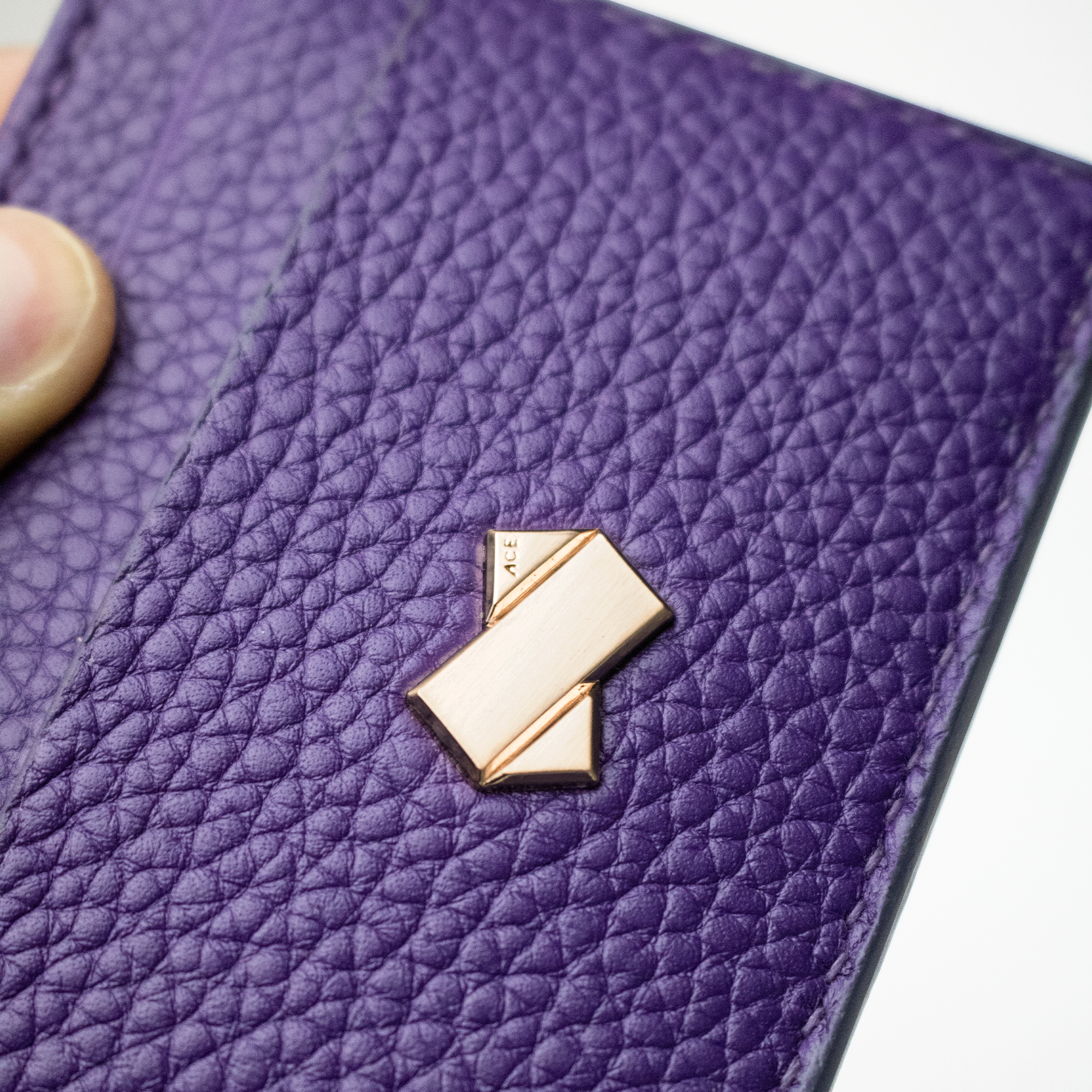 Nærbillede af det gyldne Faubret-logo på lilla præget læder – fransk kvalitet og design.