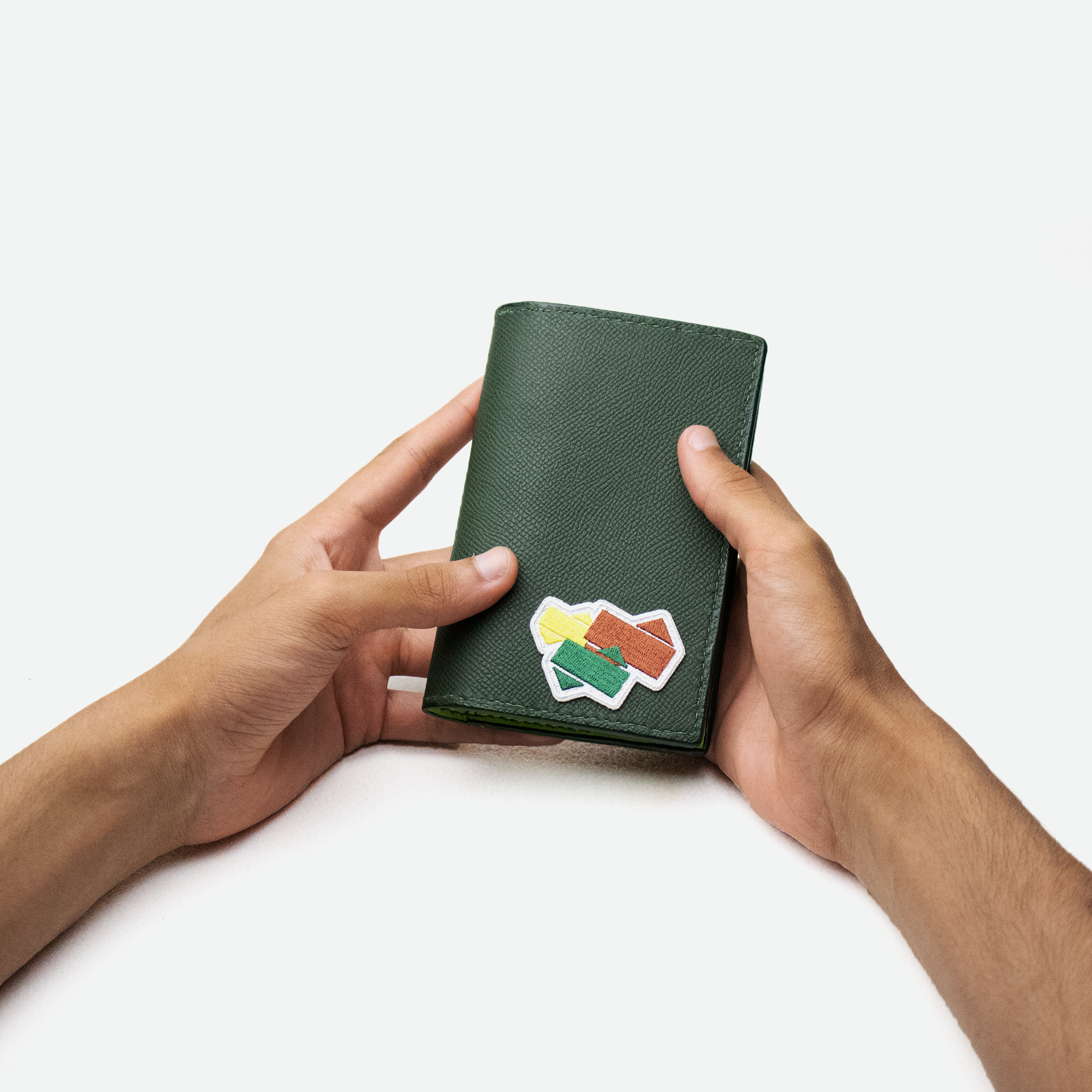 Faubret’s pascover i grynet grønt læder med broderet patch, holdt i hænderne.
