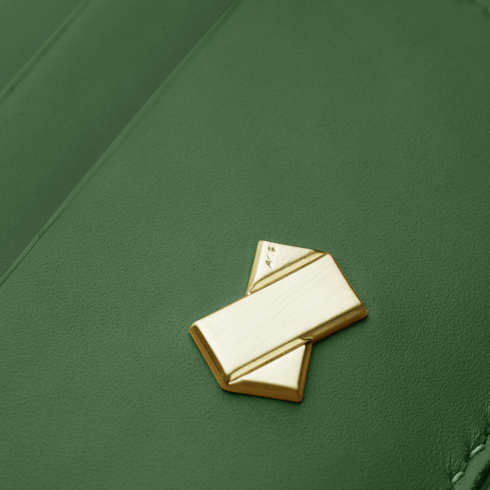 Nærbillede af Faubret-logo i børstet guld på glat grønt læder. Et tegn på eksklusivt håndværk.