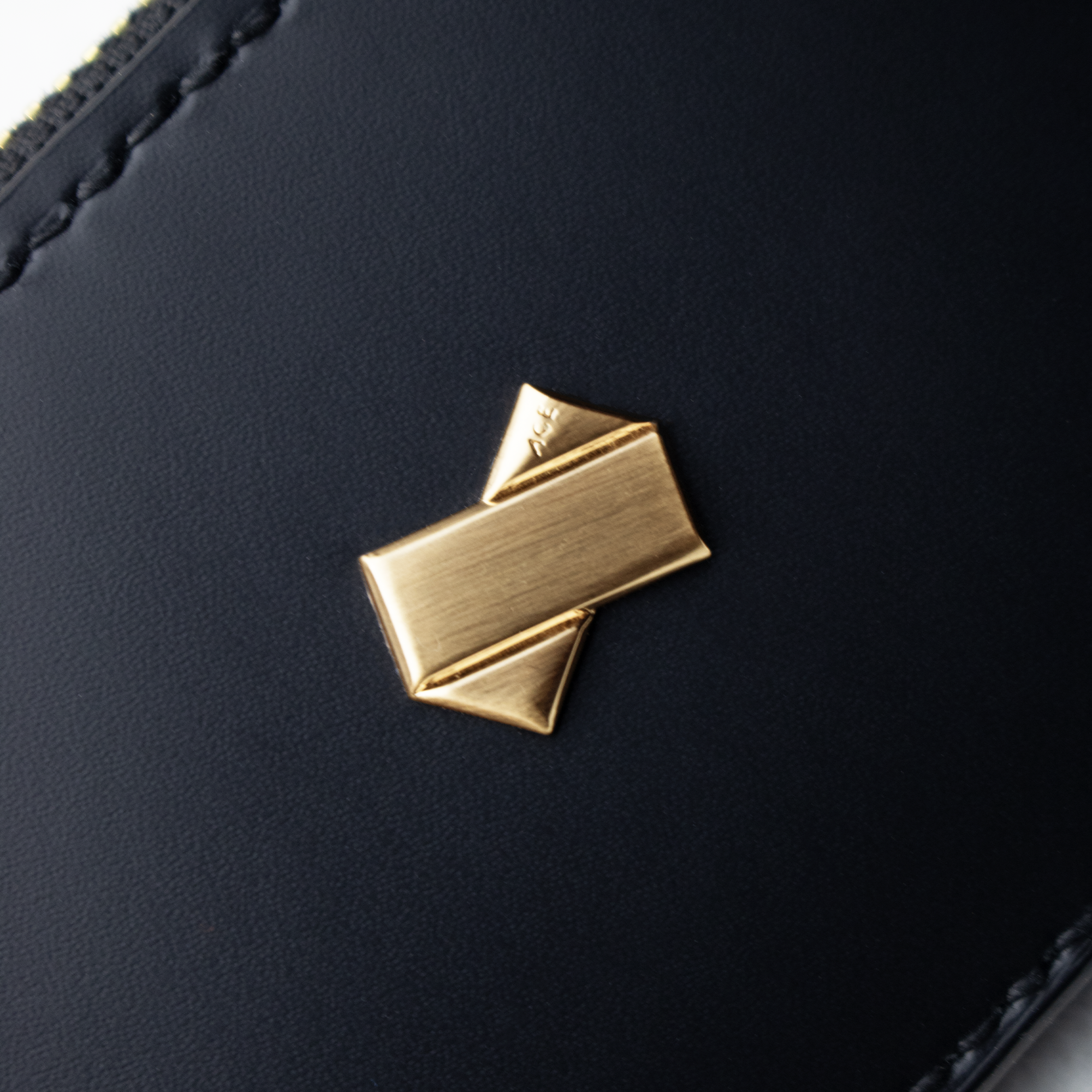 Nærbillede af Faubrets gyldne logo præget på glat sort læder.