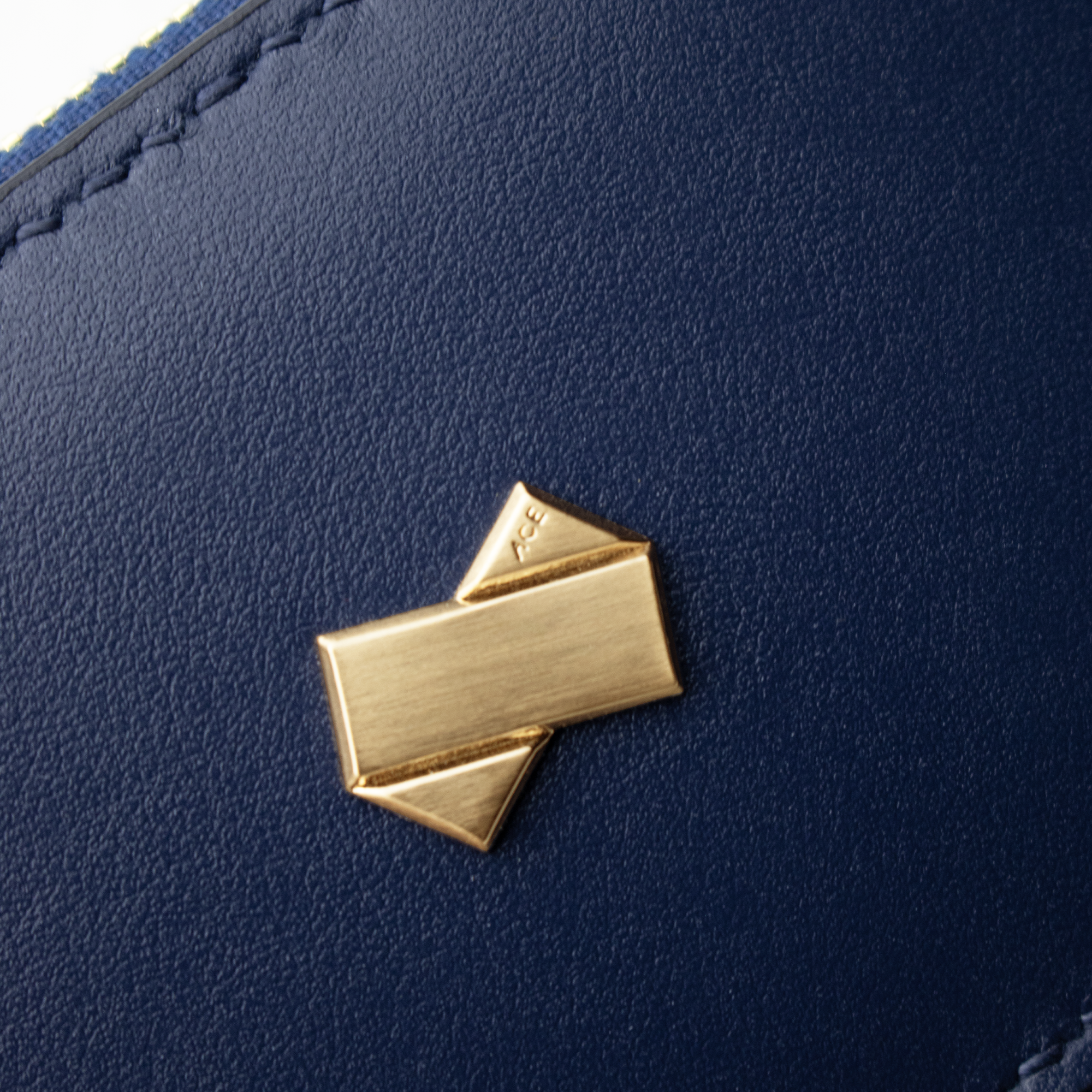 Nærbillede af Faubret-logoet i guld på blåt glat læder.