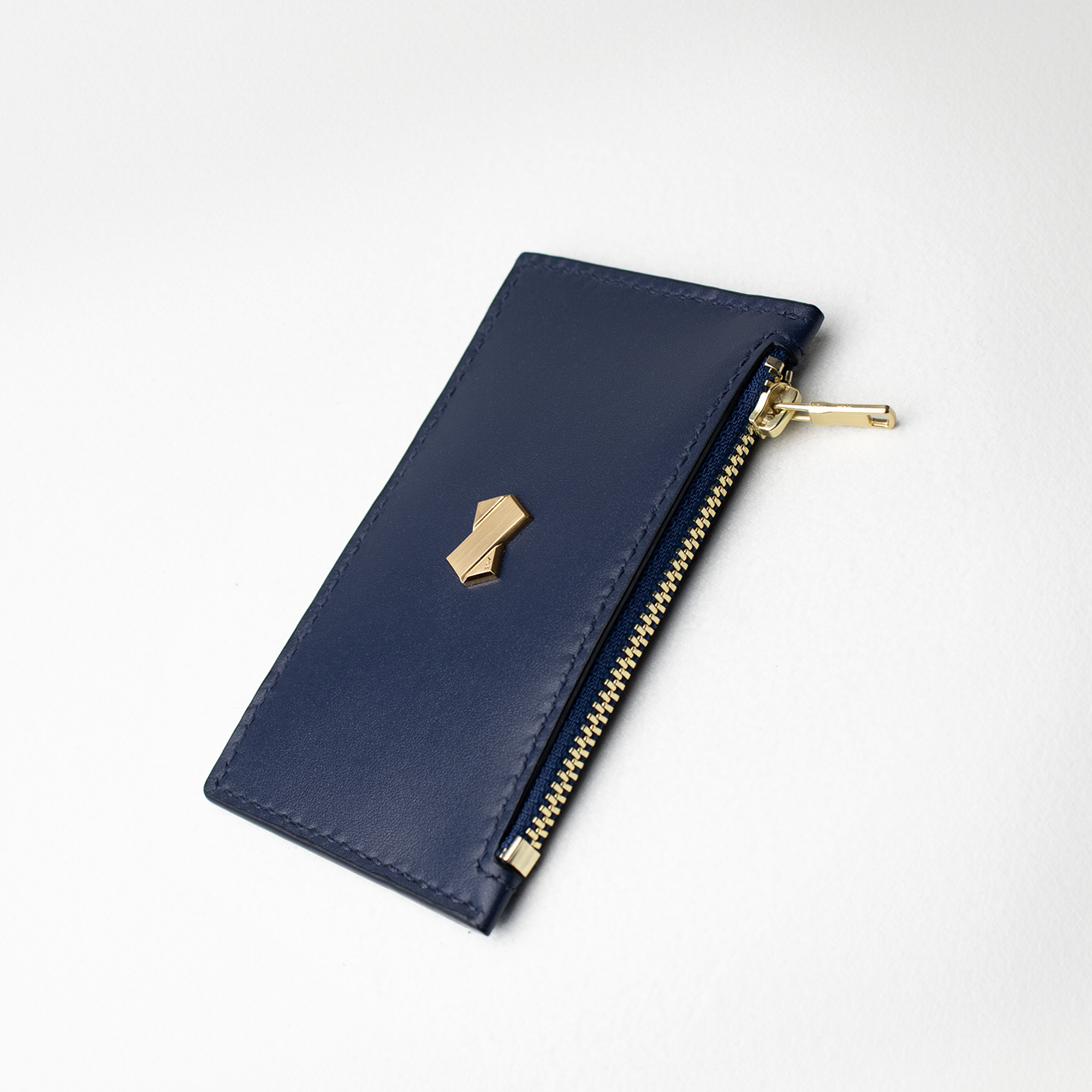 Faubret kortholder i blåt læder set skråt, med gylden lynlås og logo.