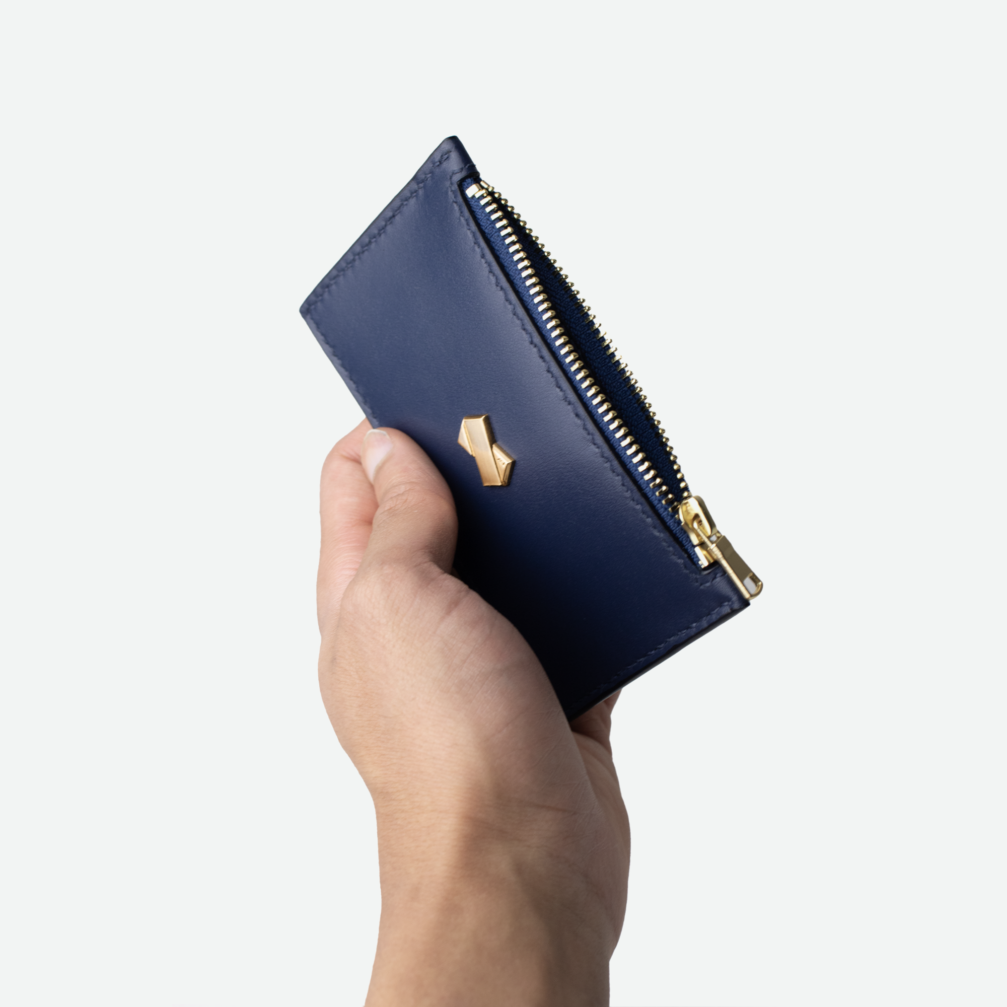 Kortholder i blåt læder fra Faubret holdt i hånden, med gylden lynlås åbnet.